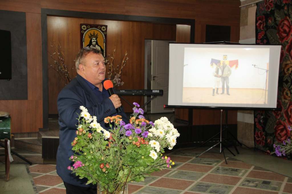 Ionel Popa vorbește la microfon, în spatele aranjamentelor florale, la lansarea volumului „Ephemer”.